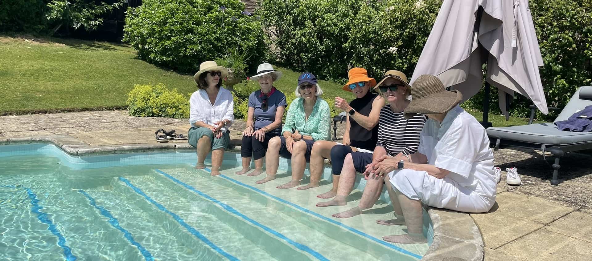 People sitting on the edge of a pool dangling their feet in the water on a hot day